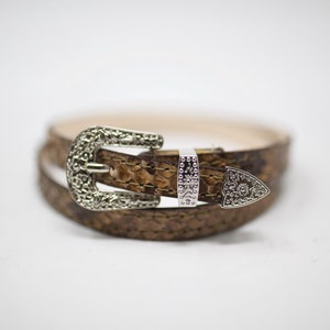 May include: A brown leather belt with a silver buckle. The buckle has a decorative design.
