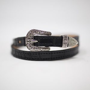 Puede incluir: Un cintur&oacute;n de cuero negro con una hebilla plateada adornada. La hebilla tiene un dise&ntilde;o floral detallado.