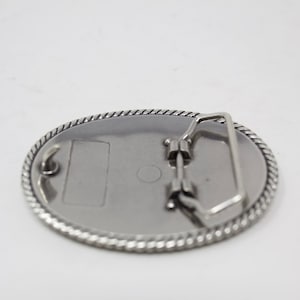 May include: Silver oval belt buckle with a rope design around the edge and a plain metal back.