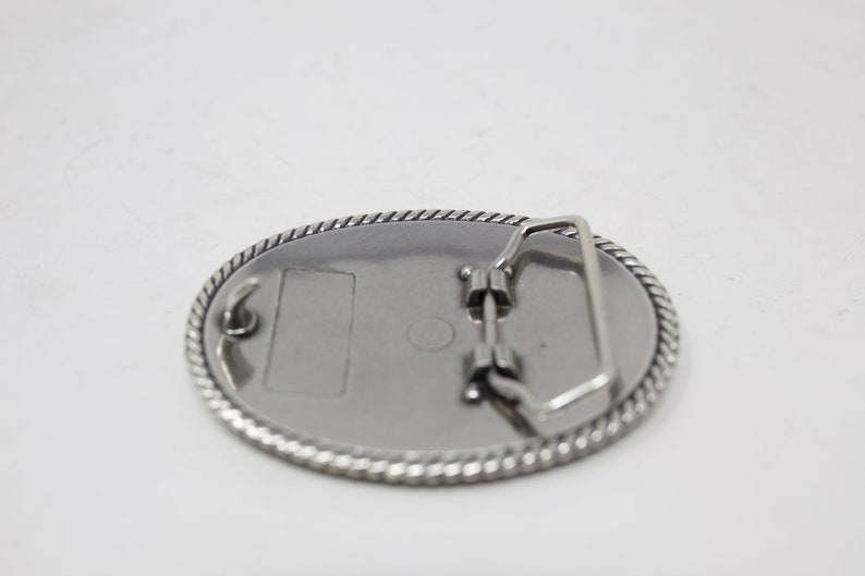 May include: Silver oval belt buckle with a rope design around the edge and a plain metal back.
