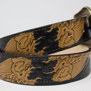 May include: A brown leather belt with a black and brown embossed design. The belt has a large, ornate brass buckle.