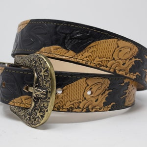 May include: A black and tan leather belt with an ornate brass buckle. The belt is embossed with a koi fish design.