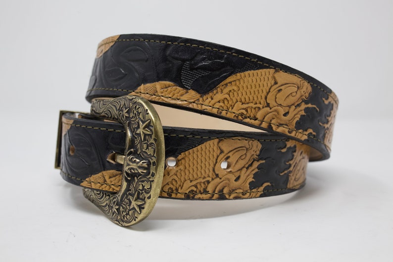 May include: A black and tan leather belt with an ornate brass buckle. The belt is embossed with a koi fish design.