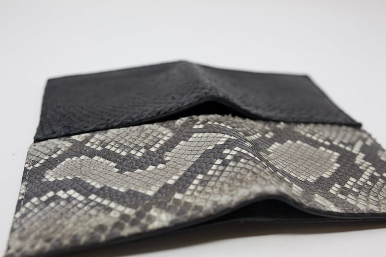 Peut inclure: Un portefeuille en cuir noir avec un motif en peau de serpent &agrave; l'ext&eacute;rieur. Le portefeuille est pli&eacute; en deux et le c&ocirc;t&eacute; en peau de serpent est face vers le haut.