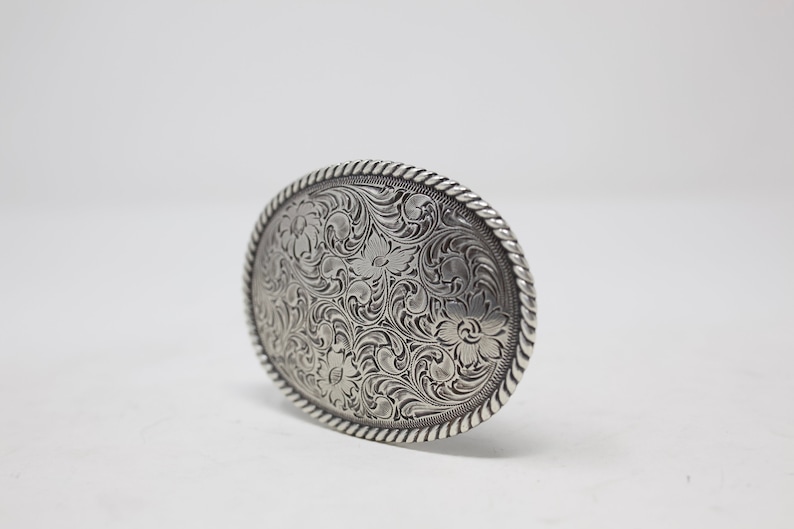 May include: Silver belt buckle with an intricate floral design.
