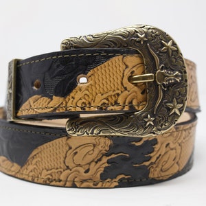 May include: A black and tan leather belt with an ornate brass buckle featuring a star design. The belt is decorated with an embossed pattern of fish and waves.