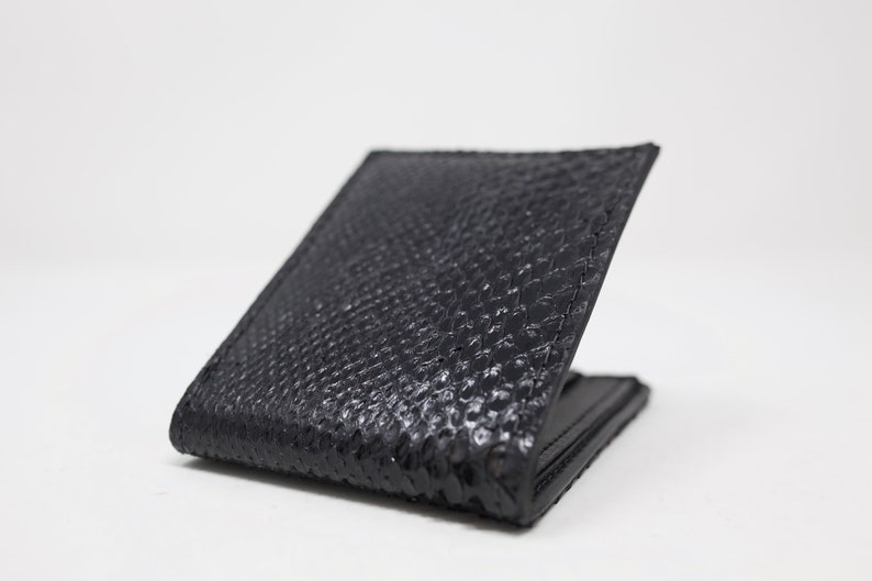 Peut inclure: Un portefeuille en cuir noir avec un motif textur&eacute; en peau de serpent.