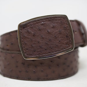 May include: A brown ostrich leather belt with a silver buckle. The buckle is rectangular with rounded corners.