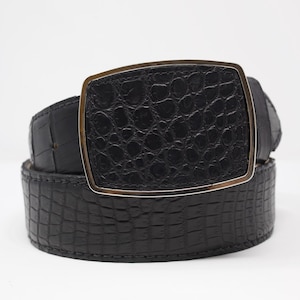 May include: A black belt with a textured, crocodile-like pattern. The belt features a large, rectangular buckle with a gold-colored frame. The belt is a fashion accessory.