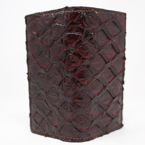 May include: A burgundy leather wallet with a snakeskin pattern. The wallet is closed and standing upright on a white surface.