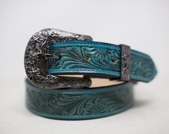 May include: A turquoise leather belt with an intricate floral design and a silver buckle. The belt is folded in half, with the buckle on top.