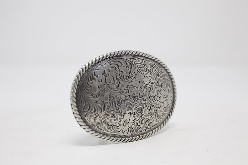 May include: Silver belt buckle with an intricate floral design.