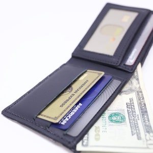 Peut inclure: Un portefeuille en cuir noir avec plusieurs fentes pour cartes et un compartiment pour billets. Le portefeuille est ouvert et contient des cartes de cr&eacute;dit et un billet de dollar.