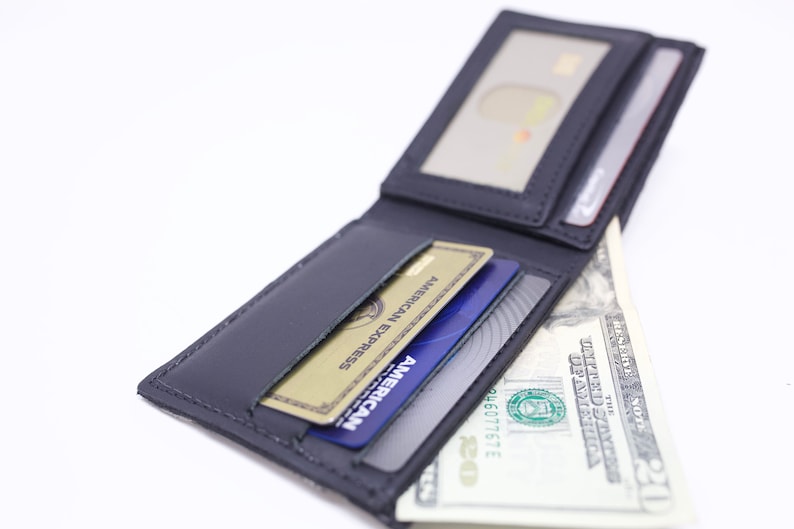 Peut inclure: Un portefeuille en cuir noir avec plusieurs fentes pour cartes et un compartiment pour billets. Le portefeuille est ouvert et contient des cartes de cr&eacute;dit et un billet de dollar.