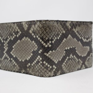 Peut inclure: Un portefeuille en cuir de serpent gris et noir avec un motif textur&eacute;.