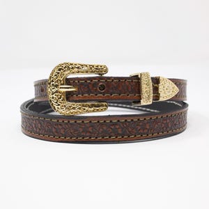 May include: A brown leather belt with a gold-colored buckle and floral embossed design. The belt has a gold-colored buckle and a matching gold-colored belt tip. The belt is approximately 1 inch wide.