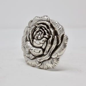 Puede incluir: Una escultura de rosa detallada, de color plateado. La escultura es una representaci&oacute;n realista de una rosa, con m&uacute;ltiples capas de p&eacute;talos y detalles intrincados. La rosa es un objeto decorativo.