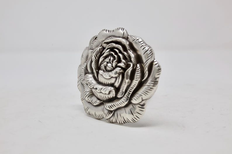 Puede incluir: Una escultura de rosa detallada, de color plateado. La escultura es una representaci&oacute;n realista de una rosa, con m&uacute;ltiples capas de p&eacute;talos y detalles intrincados. La rosa es un objeto decorativo.