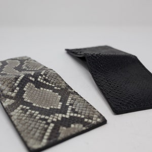 Peut inclure: Deux portefeuilles en cuir, un noir et un autre &agrave; motif de peau de serpent.
