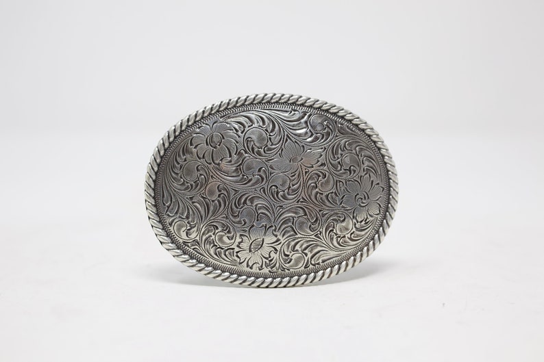 May include: Silver oval belt buckle with a detailed floral design.