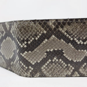 Peut inclure: Un portefeuille en cuir de serpent noir et gris avec un bord cousu.