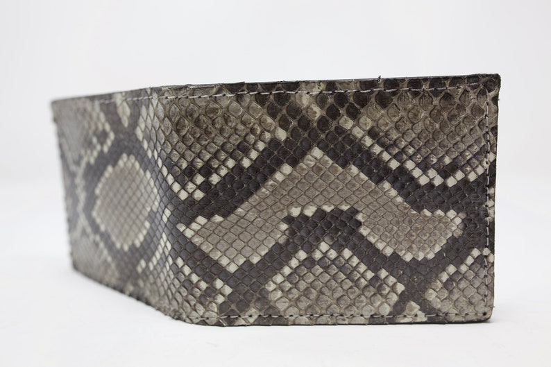Peut inclure: Un portefeuille en cuir de serpent noir et gris avec un bord cousu.