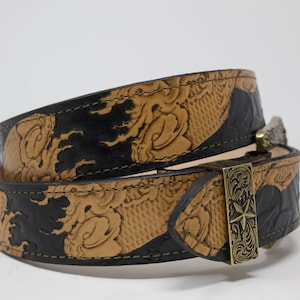 May include: A black and brown leather belt with an intricate embossed design and a silver buckle. The buckle features a star design.