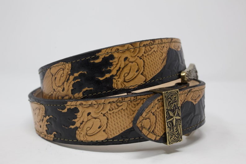 May include: A black and brown leather belt with an intricate embossed design and a silver buckle. The buckle features a star design.