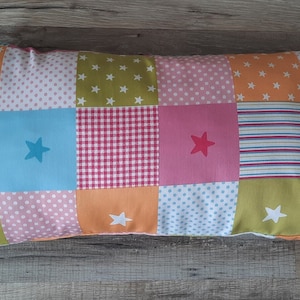 Könnte beinhalten: Ein rechteckiges Patchwork-Kissen mit verschiedenen Farben und Mustern, darunter rosa, blau, grün, orange und weiß. Das Kissen ist mit kleinen weißen Sternen verziert.