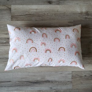 Puede incluir: Una almohada blanca con un patrón de arcoíris rosa y marrón y lunares dorados.