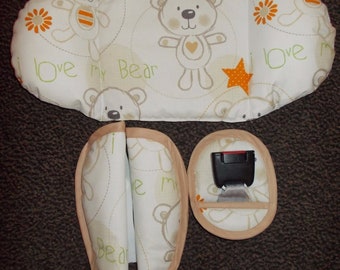 May include: A baby car seat insert set with a cream-colored fabric featuring a repeating bear pattern and the text "I love my Bear". The set includes a headrest, shoulder pads, and a buckle cover, all with a tan trim.