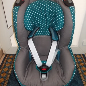 Puede incluir: Un asiento de coche gris y azul verdoso con un patrón de estrellas blancas. El asiento tiene un arnés de cinco puntos y un reposacabezas.