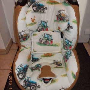 May include: A white and brown car seat cover with a tractor pattern. The cover features a variety of blue and green tractors on a white background with brown accents.