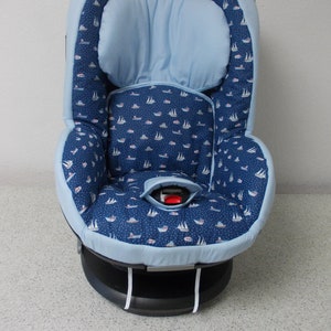 Puede incluir: Un asiento de coche para bebé azul y blanco con estampado de barcos, con un reposacabezas azul y una base negra.