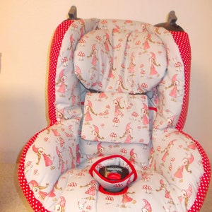 May include: A red and white car seat cover with a pattern of girls in red hoods and mushrooms. The cover has a red and white polka dot trim.