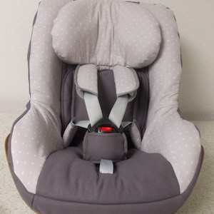 Puede incluir: Un asiento de coche gris con un patrón de lunares blancos y grises. El asiento tiene un reposacabezas y un arnés de cinco puntos.
