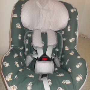 Puede incluir: Una funda para asiento de coche verde y blanca con un patrón de ardillas de dibujos animados. La funda tiene un reposacabezas acolchado y un arnés de cinco puntos.