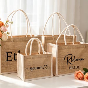 Puede incluir: Tres bolsas de yute rectangulares con ribetes de tela blanca y asas de cuerda blanca. Las bolsas presentan texto impreso en negro que incluye los nombres "Etl", "youneri" con un símbolo de corazón y "Rilena BRIDE" en fuentes cursivas y serif.