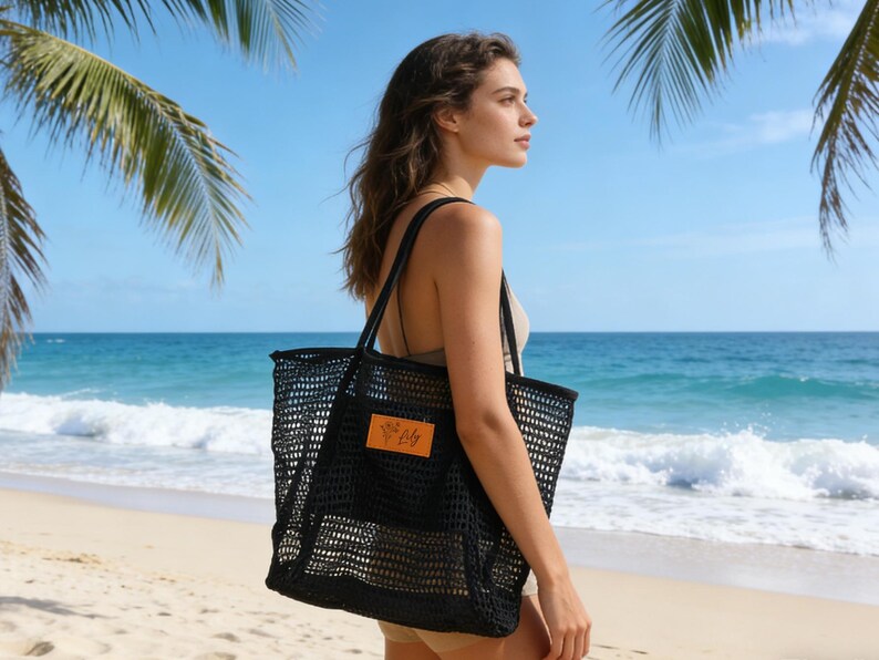 K&ouml;nnte beinhalten: Eine schwarze Netztasche mit einem rechteckigen orangefarbenen Etikett. Die Tasche wird &uuml;ber der Schulter an einem Strand mit Palmen und dem Ozean im Hintergrund getragen. Geeignet f&uuml;r Strandutensilien.