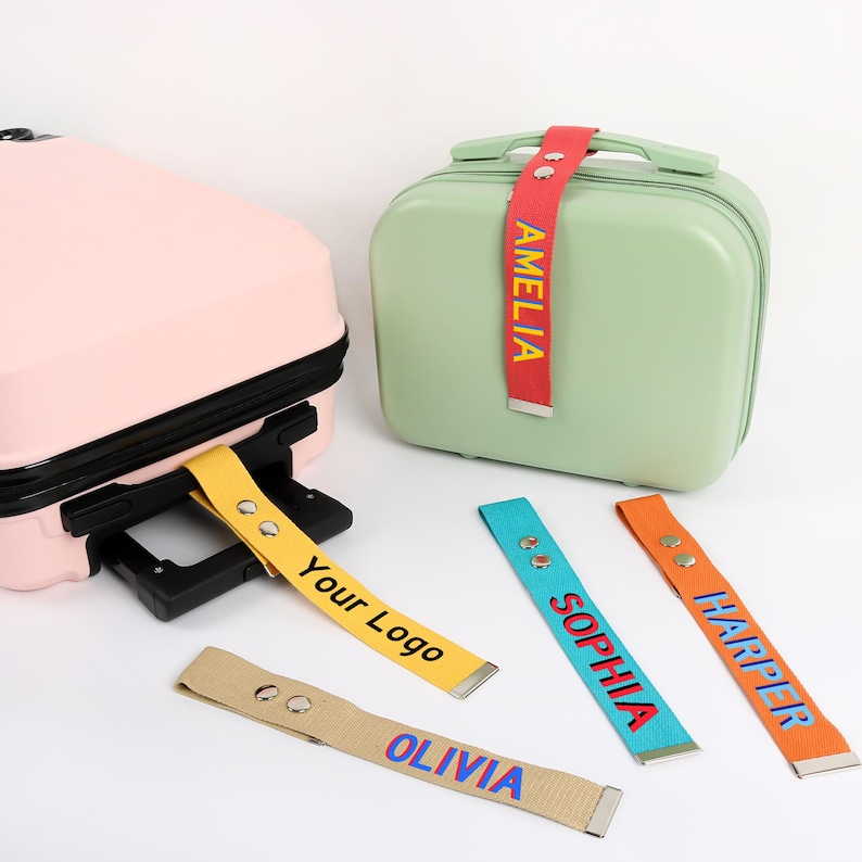 May include: A light pink suitcase and a light green suitcase with colorful luggage tags. The tags are yellow, red, blue, orange, and tan, with names and the text "Your Logo" printed on them. The tags are attached to the suitcases.