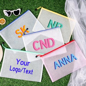 May include: Five rectangular mesh zip pouches in various colours including blue, yellow, white, mint green, and pink. Each pouch features bold, colourful lettering including SK, NP, CND, ANNA, and the text Your Logo/Text printed on the front.