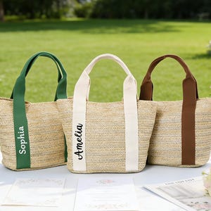 Peut inclure: Trois sacs fourre-tout en paille tressée avec des anses en tissu vert, blanc et marron. Le sac vert porte le prénom Sophia en noir, et le sac blanc porte le prénom Amelia en noir. Chaque sac possède une base structurée et une ouverture.