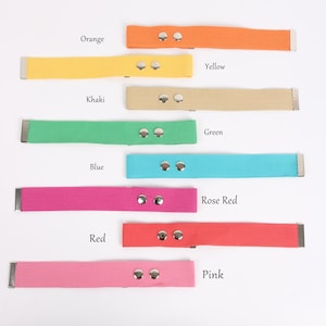 May include: A collection of colorful canvas watch straps in various shades, including orange, yellow, khaki, green, blue, rose red, red, and pink. Each strap features a metal buckle and two silver rivets. The colors are labeled with text.