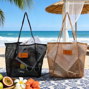 Pode incluir: Duas sacolas de rede, uma preta e outra bege, em uma toalha de praia. A sacola preta tem alças pretas e uma pequena etiqueta de couro com "Lily". A sacola bege tem alças bege. Ambas as sacolas contêm itens.