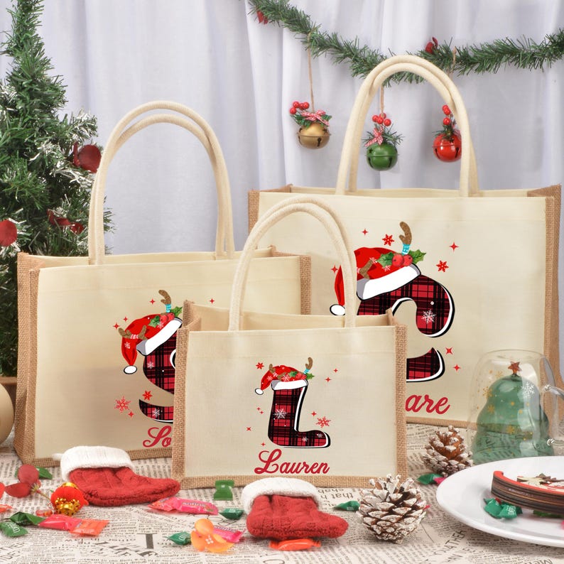 May include: Three burlap tote bags with Christmas-themed designs. The bags are decorated with red and black plaid stockings, Santa hats, and reindeer antlers. The bags are personalized with the names "Lauren", "So", and "are".