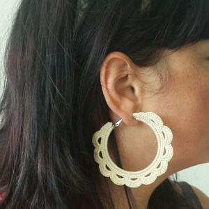 May include: A pair of large, white crocheted hoop earrings. The earrings are made of a delicate, lacy material and have a scalloped edge.