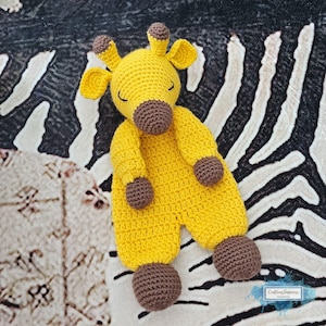 Könnte beinhalten: Ein handgefertigtes, gelbes Häkeltier in Form einer Giraffe mit braunen Akzenten. Die Giraffe hat eine braune Schnauze, Ohren und Füße. Das Spielzeug liegt auf einer schwarz-weißen Zebra-Oberfläche. Ein weiches Spielzeug für Babys und Kinder.