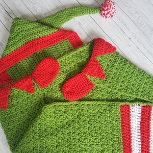 May include: Green and red crocheted baby blanket with a hood and elf shoes. The blanket has a striped pattern on one side.