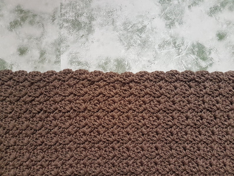 K&ouml;nnte beinhalten: Eine braune geh&auml;kelte Decke mit einem gewellten Rand.