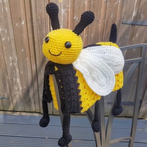 May include: A crocheted bee toy with black and yellow stripes, white wings, and a smiling face.